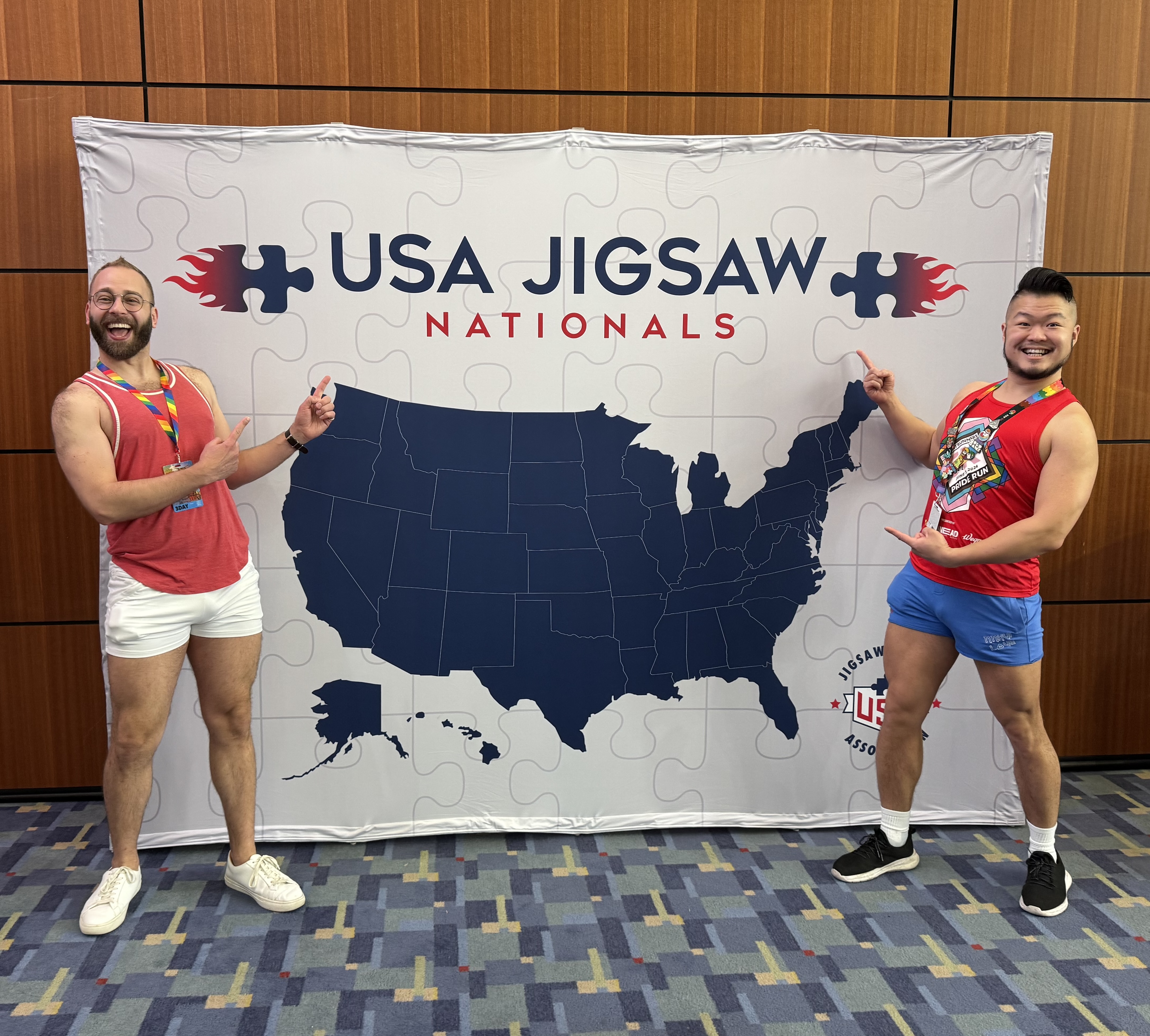 A photo of Michael and Andrew standing in front of a USA Jigsaw Nationals banner, pointing gleefully.